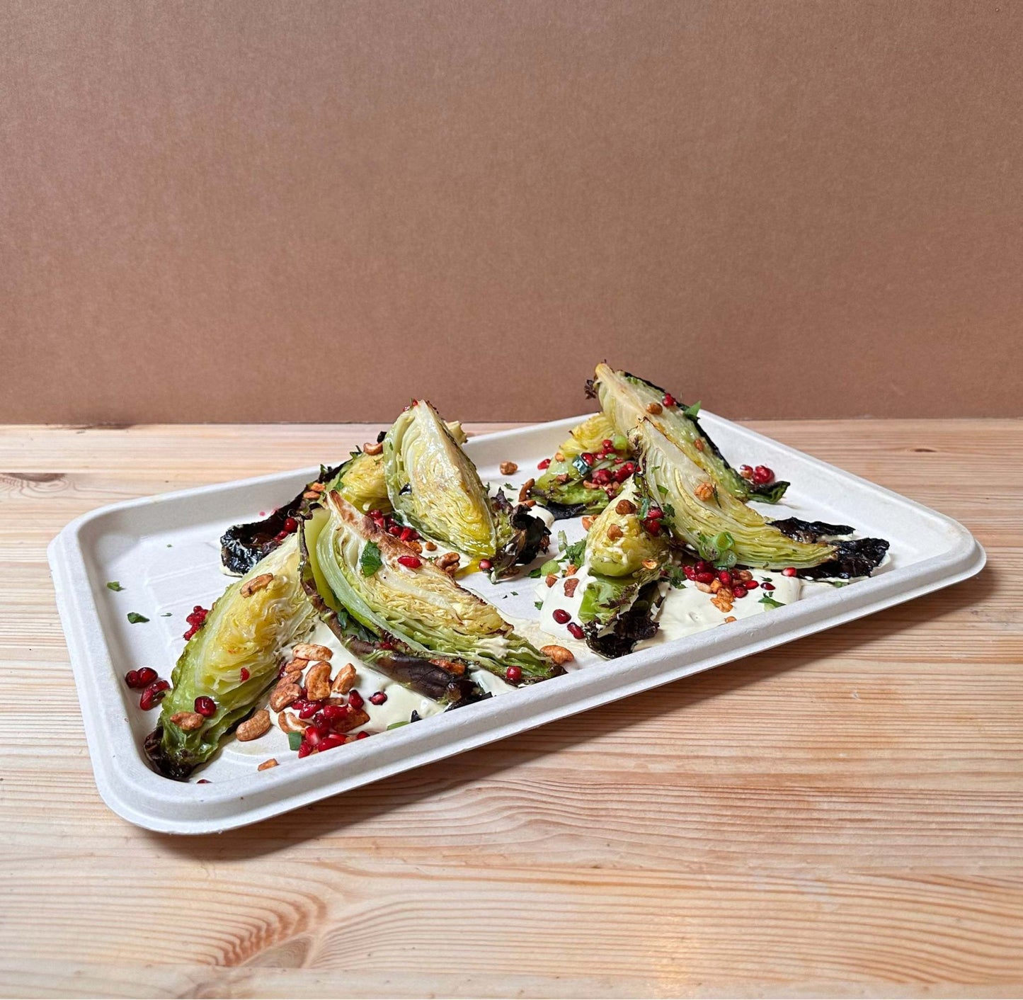 Vegan Baked cabbage, topped with tahini amba sauce, chopped Medjool dates, spiced cashew nuts, pomegranate seeds, scallions and lemon zest.