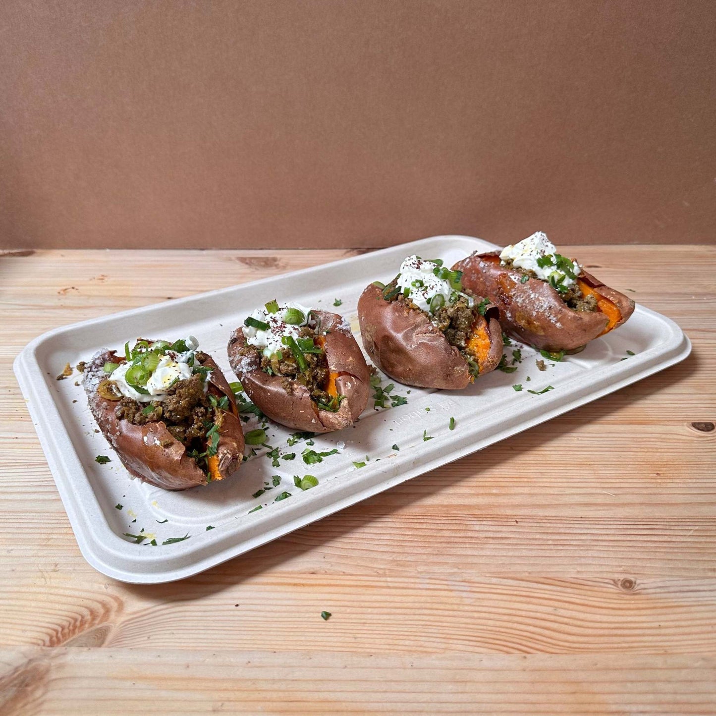 A platter of whole baked sweet potato filled with onion sumac labneh sauce, Shouk style beef and lamb mince mix, radish, scallions and parsley