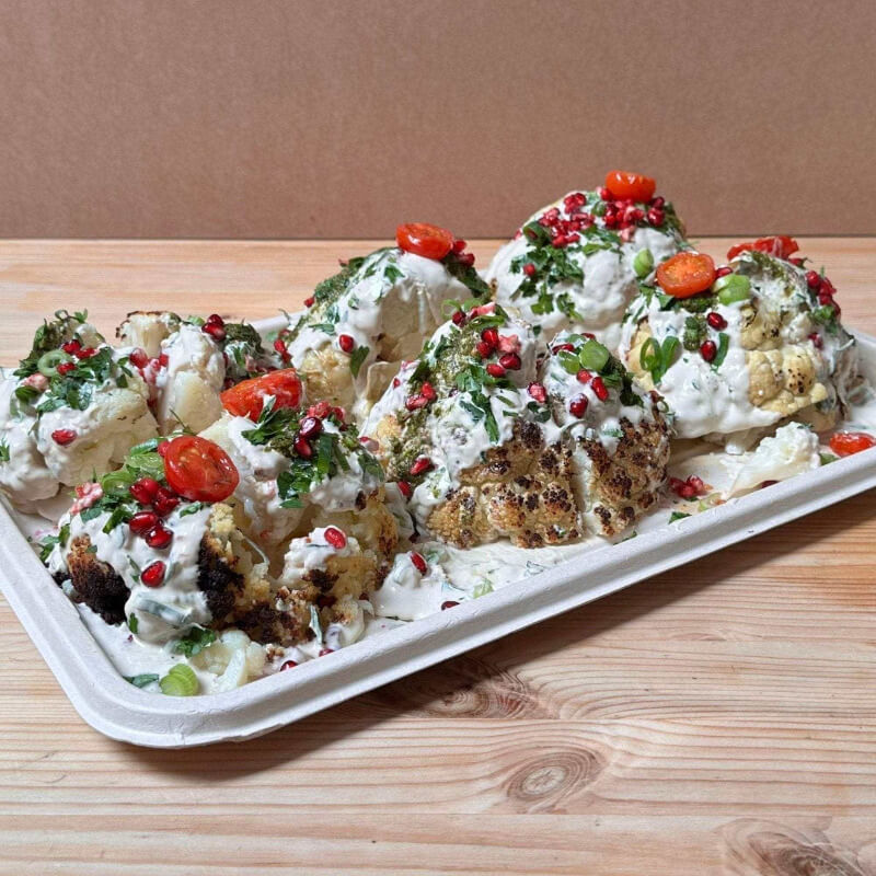 Platter of roasted cauliflower with herbs and pomegranate seeds on a wooden surface