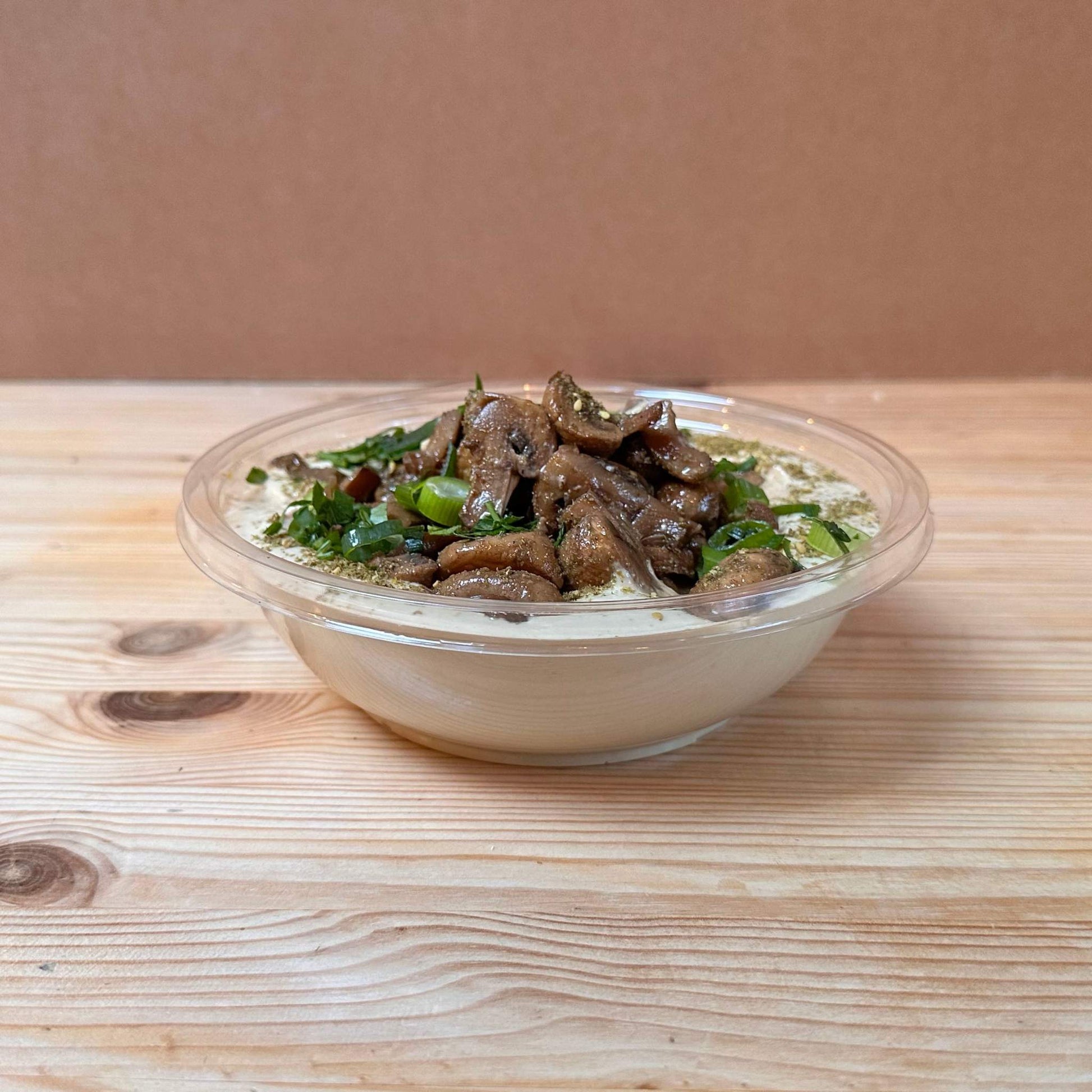 Shouk's Homemade Hummus topped with creamy tahini, a mix of grilled seasoned mushrooms, and caramelized onions